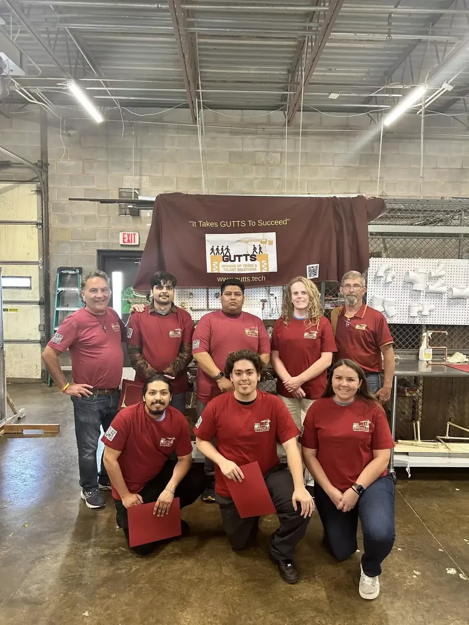 HVAC trainees in matching red shirts holding their certificates in a training workshop